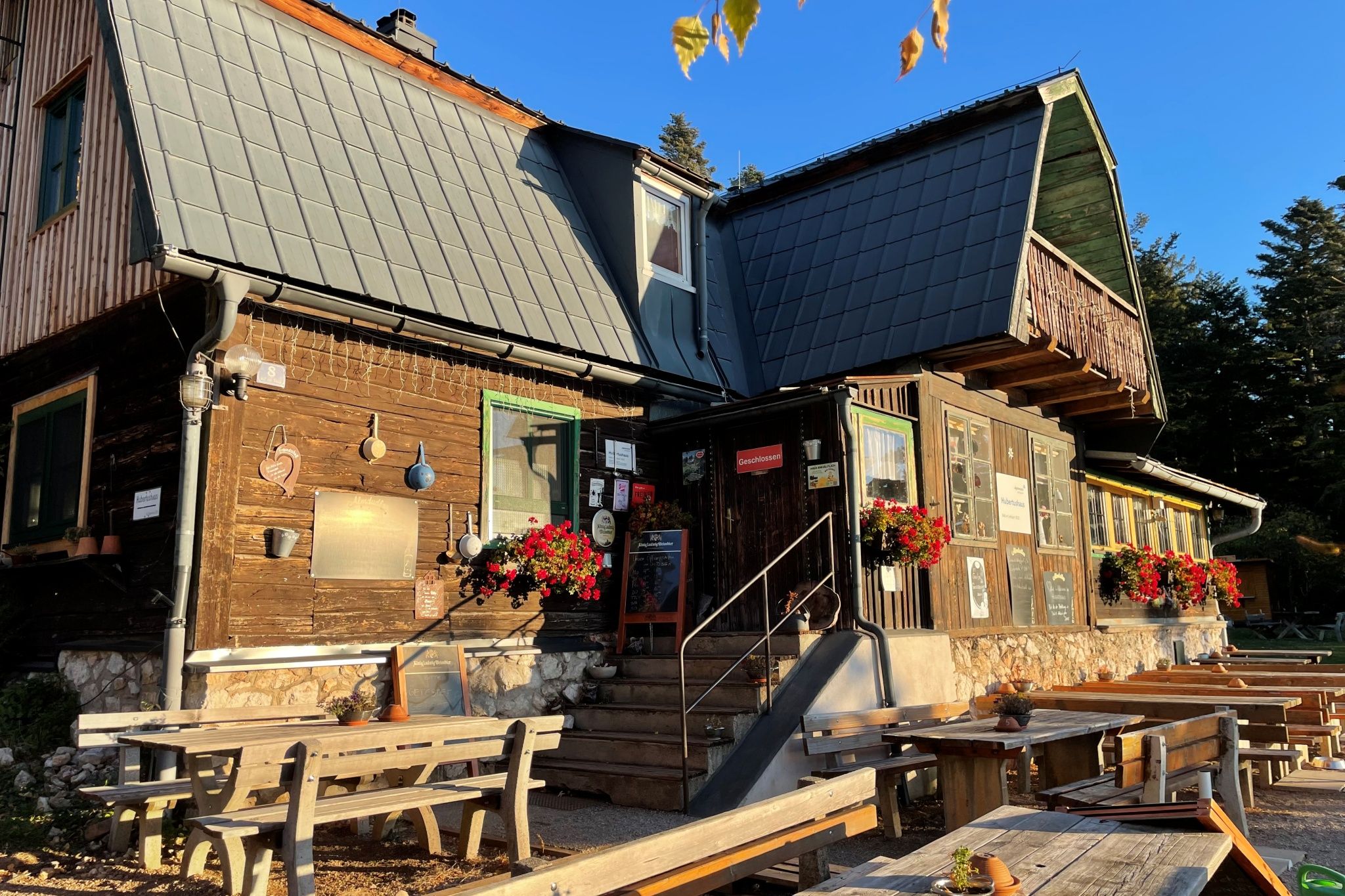 A rustic wooden house with flowers and benches outside in the sunshine.