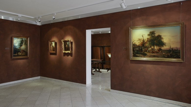 Innenansicht eines Museums mit Gemälden an braunen Wänden.